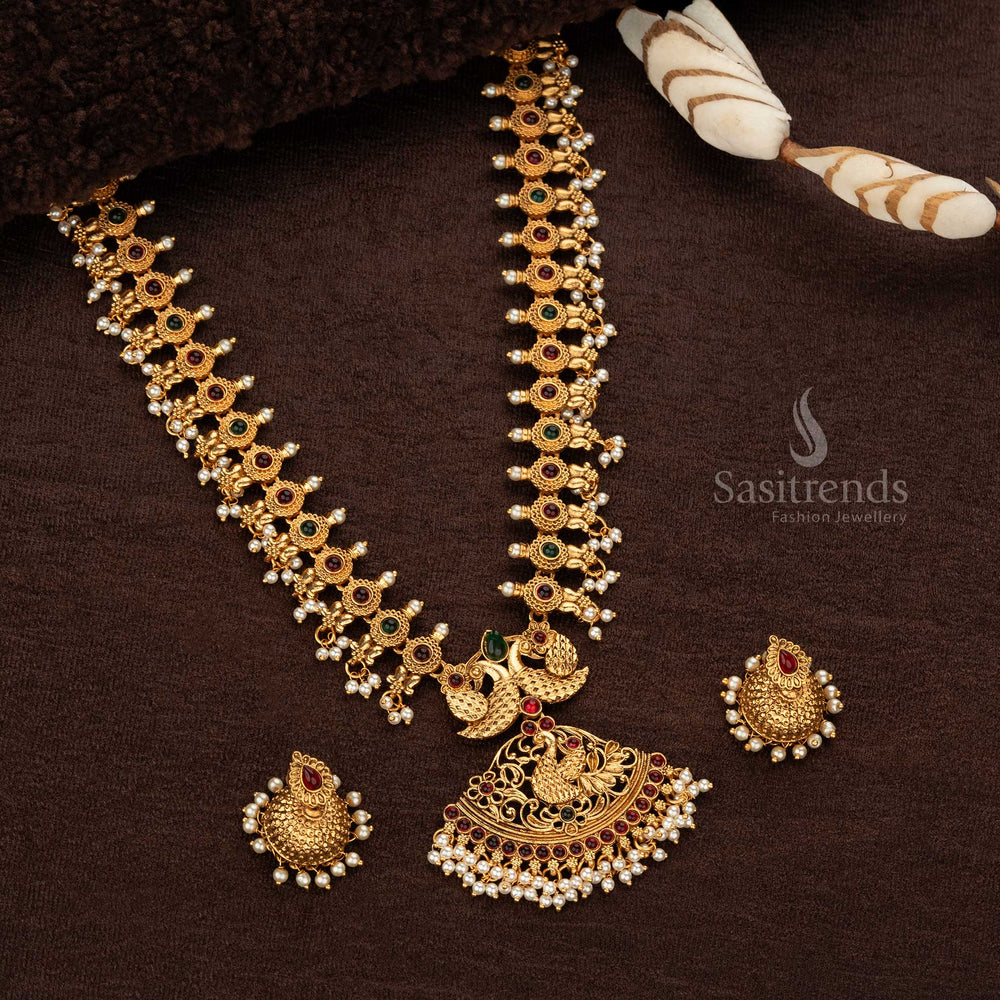 Regal ruby and green stone-accents on a matte gold-plated temple peacock long haram necklace, perfect for grand wedding ceremonies - Sasitrends