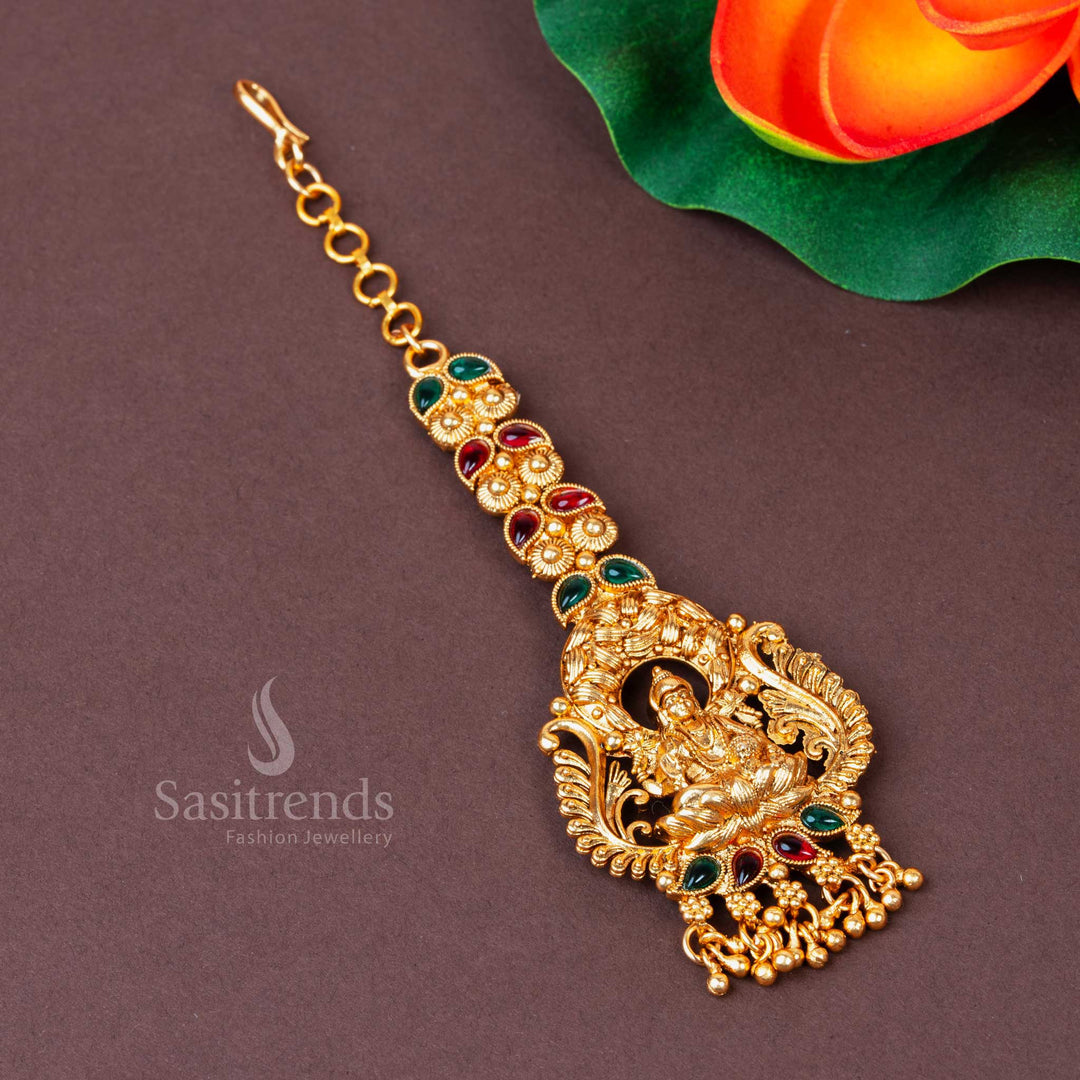 Timeless Temple Jewelry Style Maang Tikka in Matte Gold Plating, Showcasing Goddess Lakshmi’s Blessings with Ornate Ruby-Green Stones  - Sasitrends