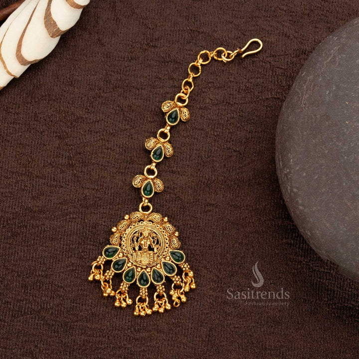 Green matte gold plated tear-drop synthetic stone maang tikka with Lakshmi motif and intricate floral patterns - Sasitrends