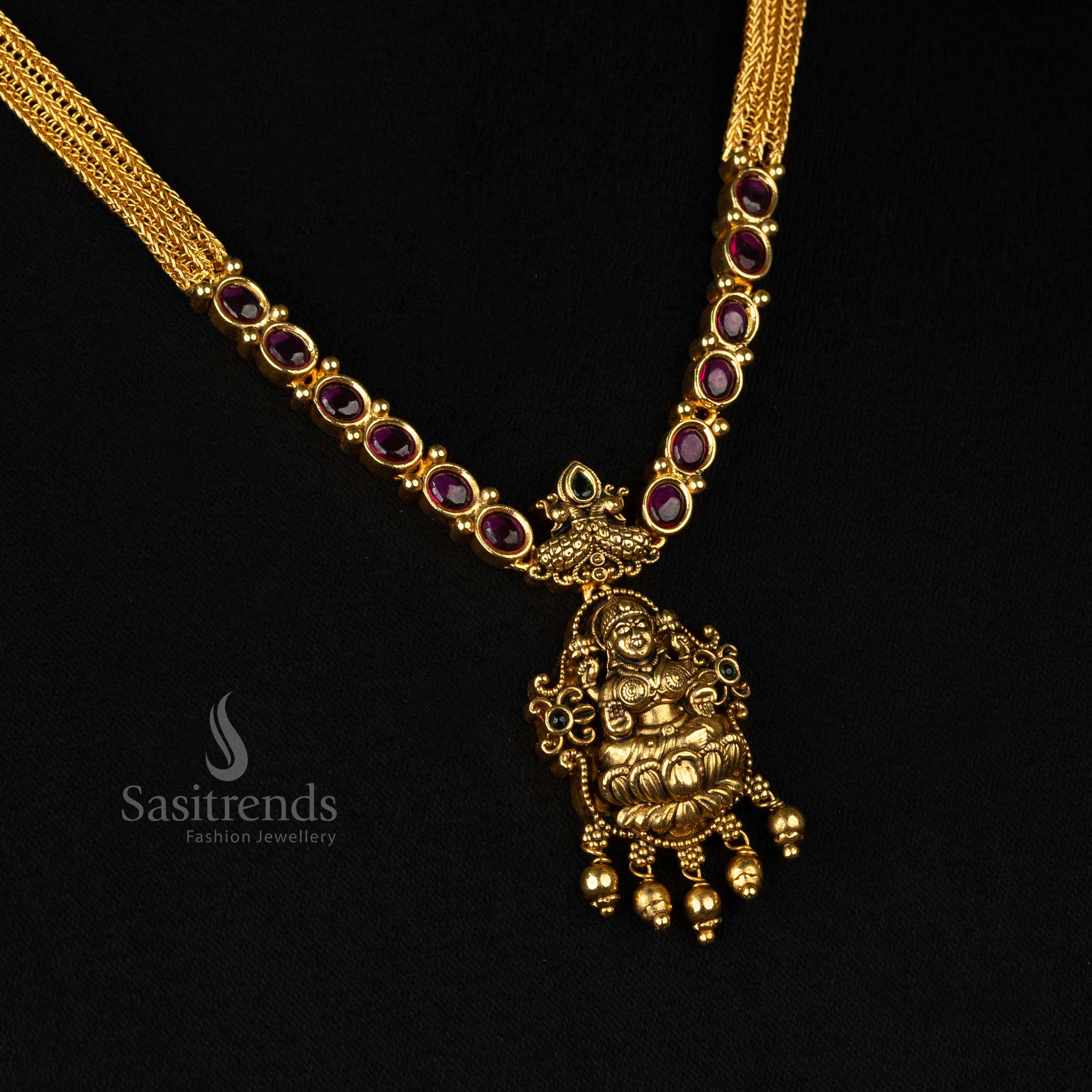 Splendid temple-style matte gold plated necklace set adorned with an ornate Goddess Lakshmi pendant, dual peacock artwork, and exquisite ruby stone embellishments - Sasitrends