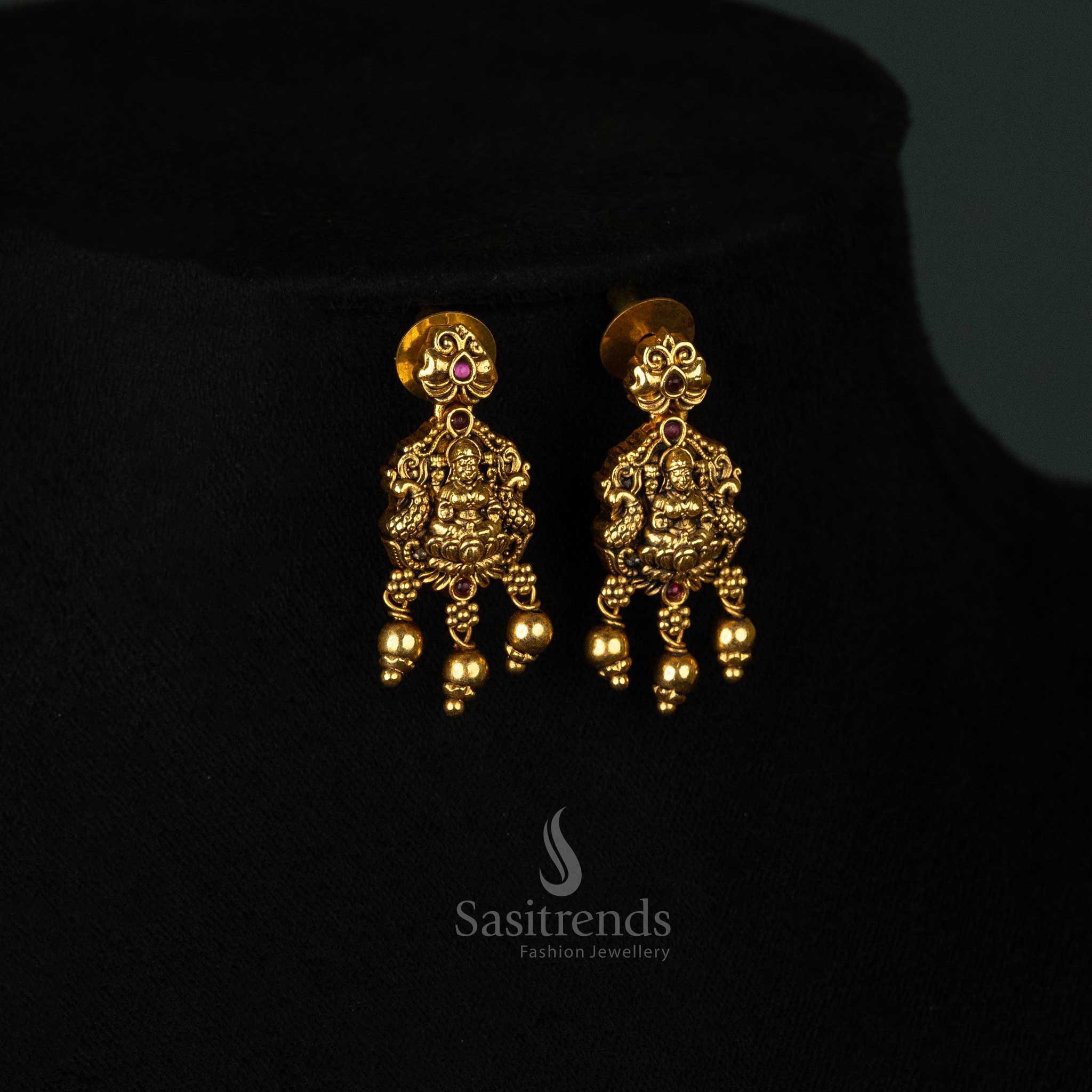 Divine matte gold plated temple earrings set adorned with a beautifully crafted Goddess Lakshmi pendant, dual peacock motif, and radiant ruby AD stones - Sasitrends