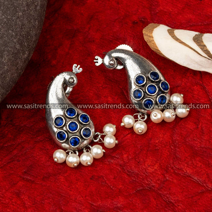 Silver peacock-shaped earrings with circular patterns and pearl drops on a red background