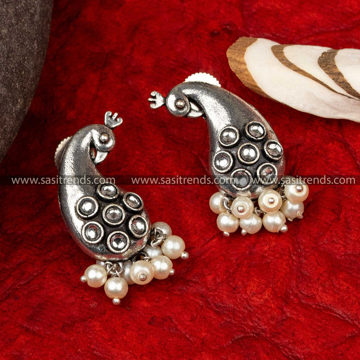 Silver earrings with peacock motif, red stone accents, and pearls, on red fabric