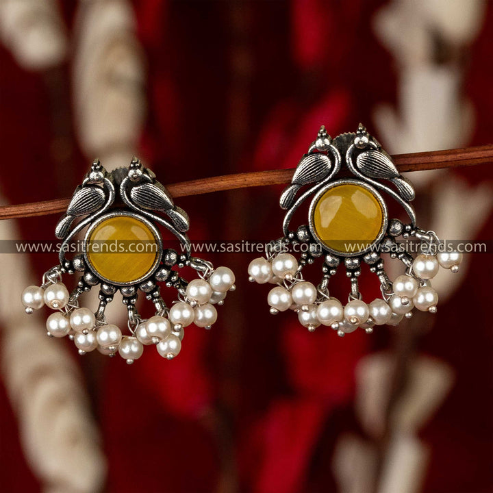 Silver peacock-shaped earrings with circular patterns and pearl drops on a red background