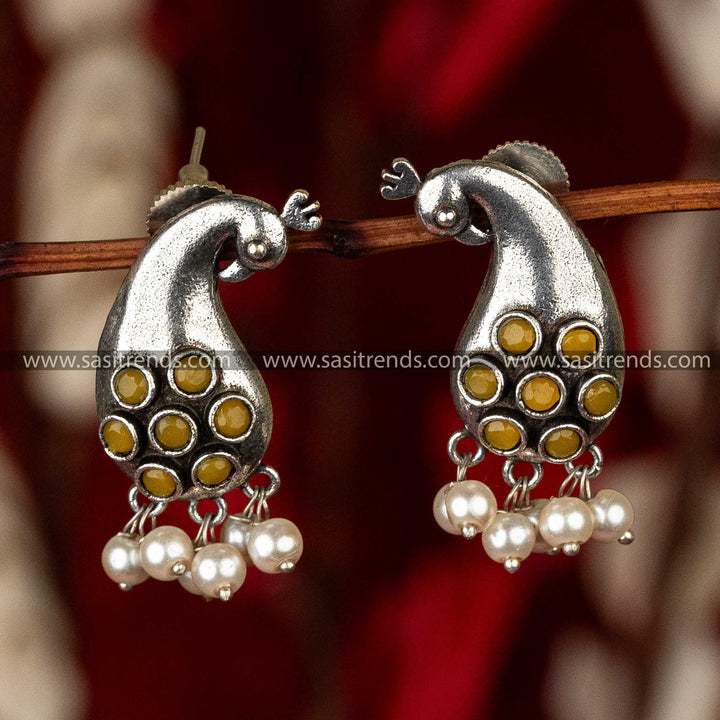 Earrings featuring a peacock design with yellow stones and pearl adornments, red background