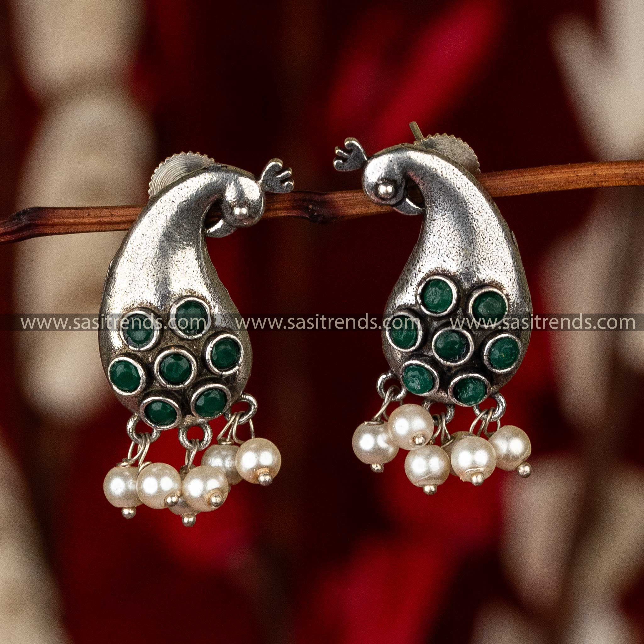 Oxidized peacock earrings with green stones and pearls on a red textile background