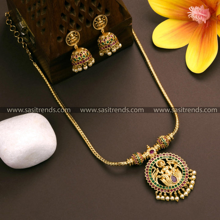 Traditional Lakshmi pendant necklace with jhumkas in matte gold finish, embellished with ruby and green American diamond stones