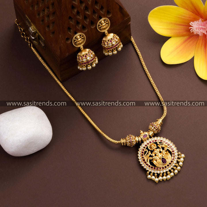 Lakshmi pendant necklace with jhumkas in matte gold plating, adorned with white and ruby American diamond stones and pearl drops 