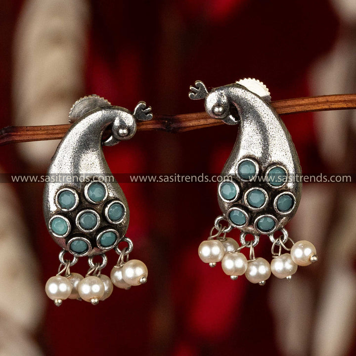 Peacock silhouette earrings with teal stones and pearls, presented on red fabric